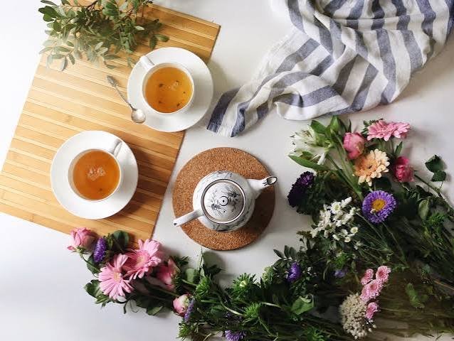 Two cups of herbal tea with a teapot and fresh flowers on a white table