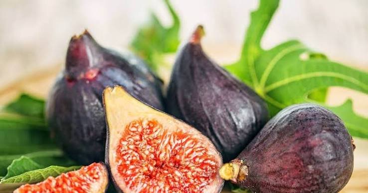 Fresh purple figs, one cut in half, with green fig leaves